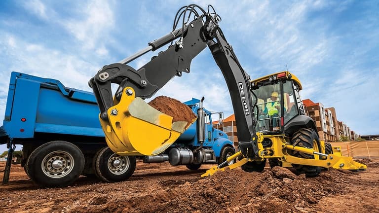 A 410P Backhoe loading dirt into a blue dump truck. | 4re Equipment