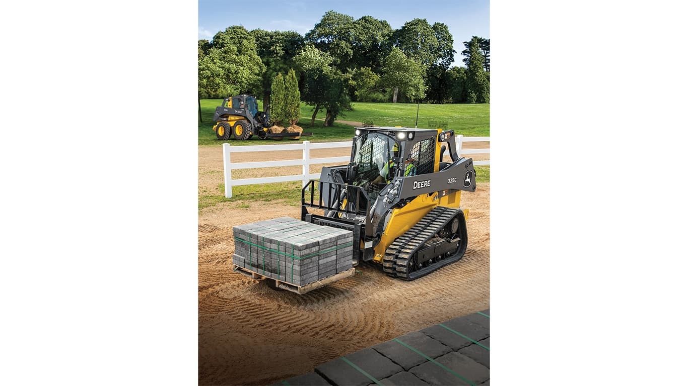 A 325G Compact Track Loader with pallet attachment moves a pallet of bricks. A 332G skid steer with nursery fork attachment moves two trees in the background. | 4re Equipment | ID: 325gxt