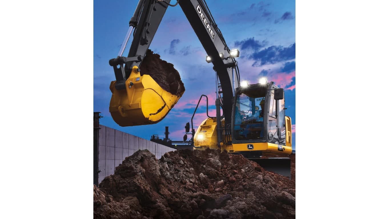 A 135P-Tier Excavator with headlights scooping dirt from a pile at a worksite with sunset in the background. | 4re Equipment | ID: 135PEXFT4