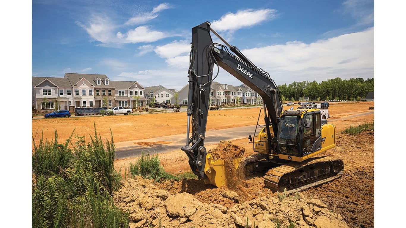 A 160P-Tier Excavator moving dirt at a worksite with a housing development in the background. | 4re Equipment | ID: 160PEXFT4