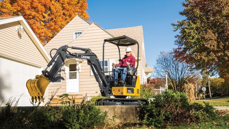 Man using a 17G excavator to move landscaping in front of a house. | 4re Equipment