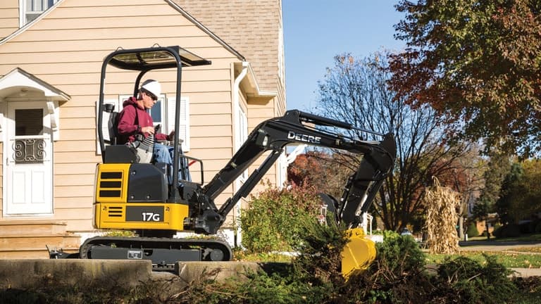Man using 17G excavator to dig up a bush in front of a house. | 4re Equipment