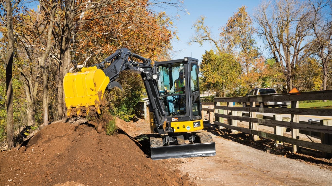 26G Excavator dropping topsoil into a stockpile on a sidewalk in front of a wooden fence. | 4re Equipment | ID: 026gxff