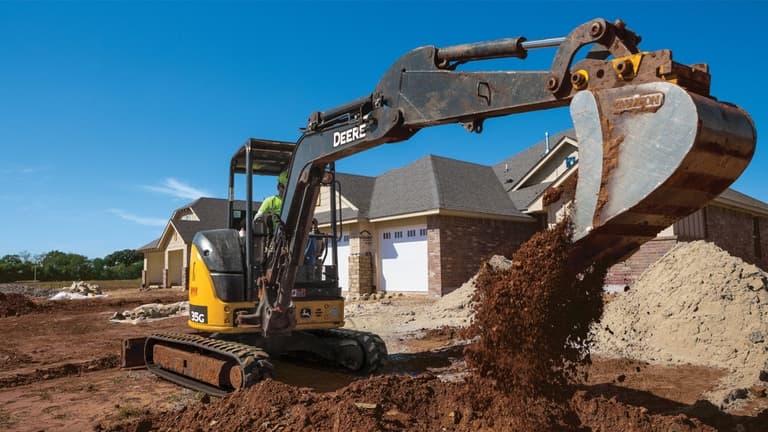 A 35G Excavator dumps topsoil into a pile in front of a housing development | 4re Equipment