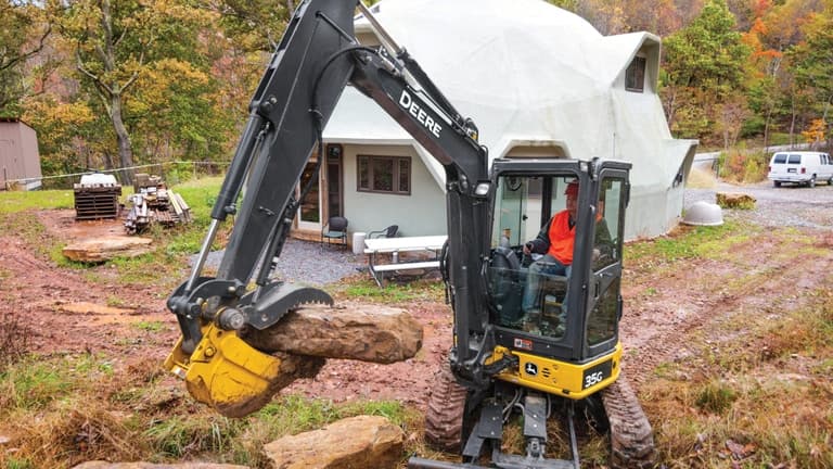 A man using a 35G Excavator to move large rocks in front of a house. | 4re Equipment