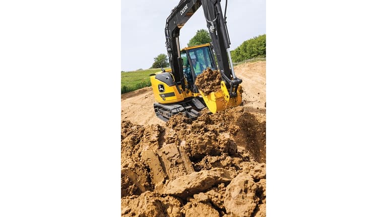 An operator using a 75P-Tier Excavator to scoop dirt at a worksite with grass and trees in the background. | 4re Equipment