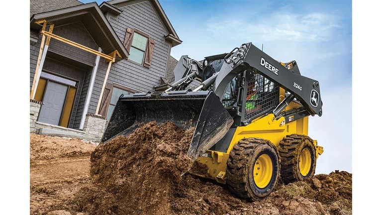 A 324G Skid Steer dumps dirt at a worksite in front of a house. | 4re Equipment